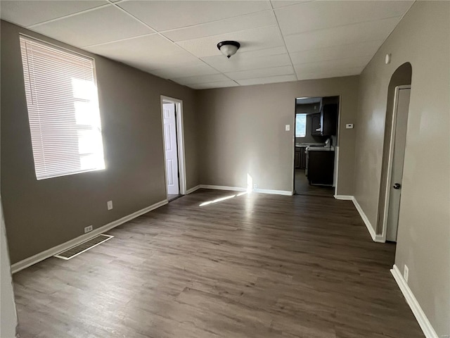 unfurnished room with visible vents, baseboards, arched walkways, a drop ceiling, and dark wood-type flooring