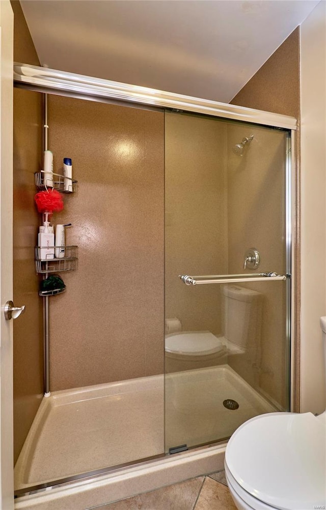 bathroom featuring tile patterned flooring, a shower with shower door, and toilet