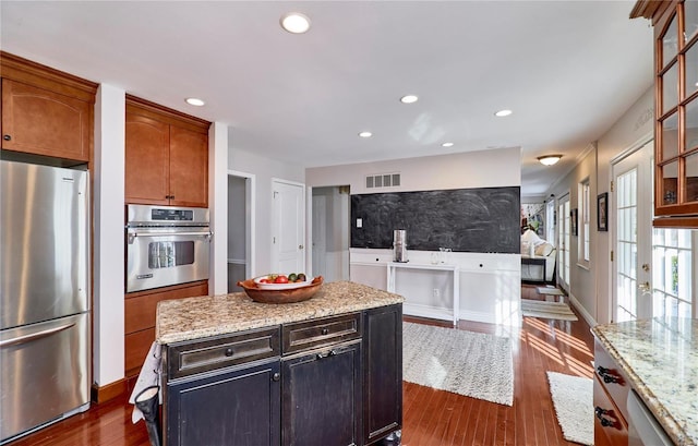 kitchen with light stone countertops, appliances with stainless steel finishes, a center island, and dark hardwood / wood-style flooring