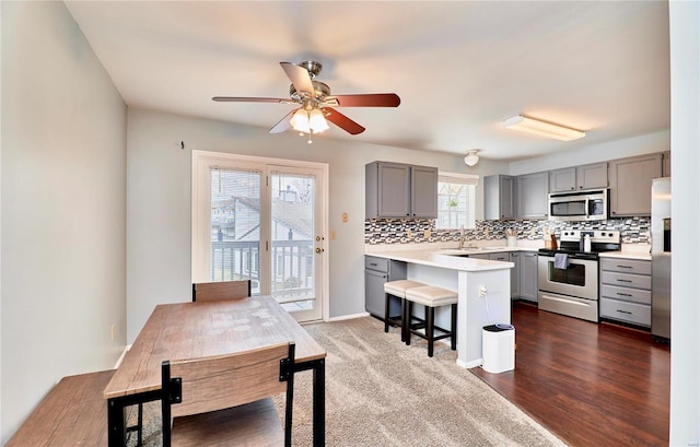 kitchen featuring gray cabinets, a breakfast bar area, appliances with stainless steel finishes, decorative backsplash, and kitchen peninsula