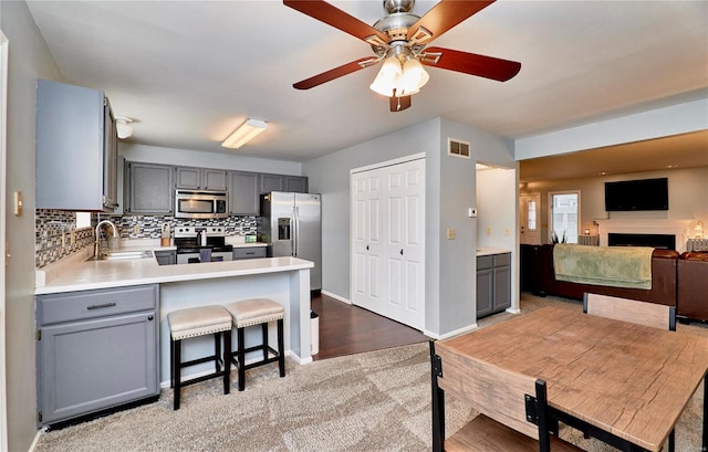 kitchen with sink, gray cabinets, appliances with stainless steel finishes, a kitchen bar, and kitchen peninsula