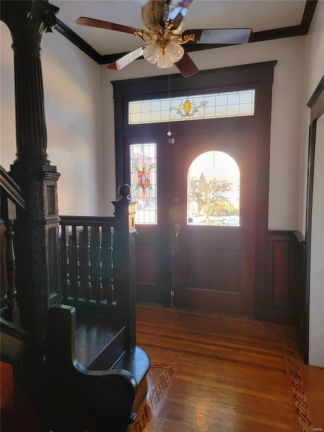 entryway featuring wood finished floors, a wainscoted wall, crown molding, and ceiling fan