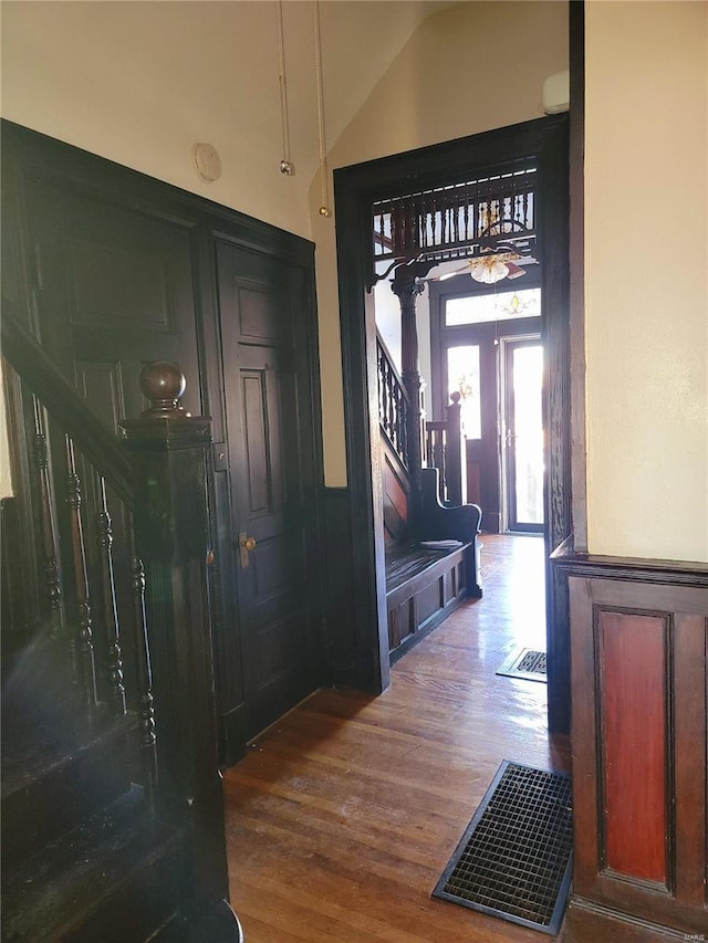 entryway featuring a wainscoted wall, lofted ceiling, stairway, wood finished floors, and ornate columns