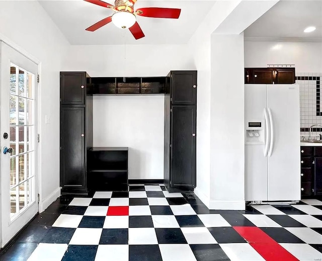 kitchen with white refrigerator with ice dispenser, baseboards, ceiling fan, dark floors, and a sink