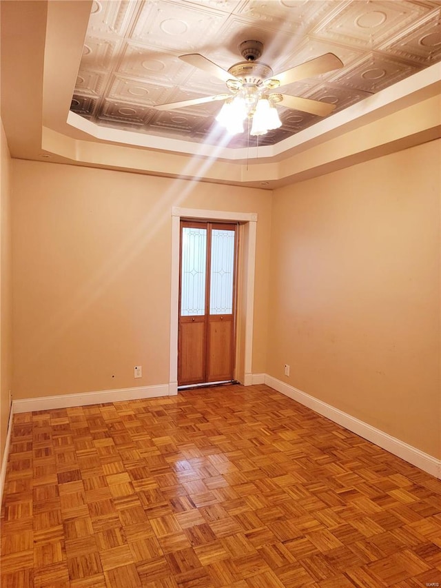 empty room featuring a tray ceiling, baseboards, and a ceiling fan