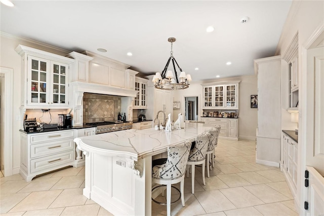 kitchen featuring decorative light fixtures, light tile patterned flooring, white cabinets, and a center island with sink