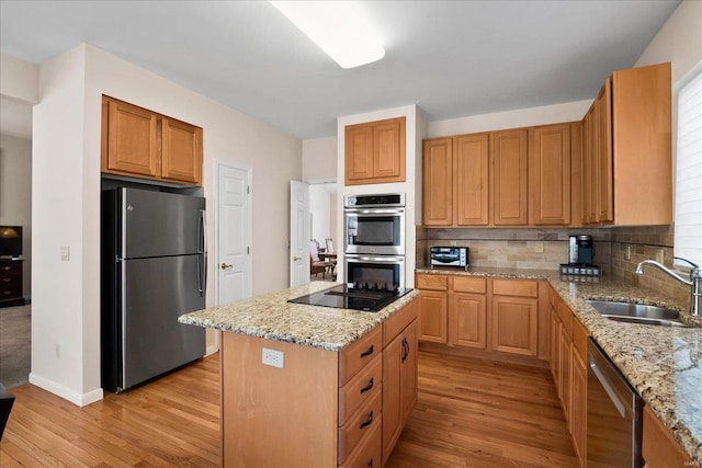 kitchen with light stone counters, stainless steel appliances, tasteful backsplash, light wood-style flooring, and a sink