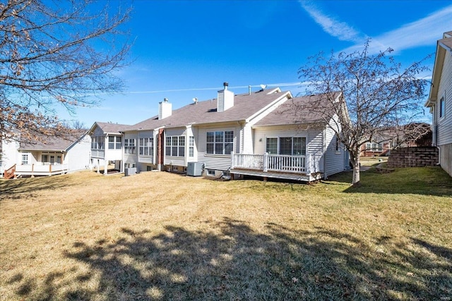 back of property with a deck, a chimney, cooling unit, and a lawn