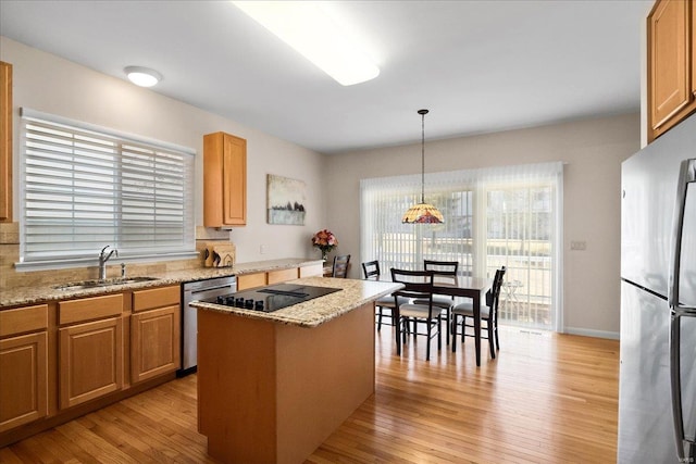 kitchen featuring stainless steel appliances, a kitchen island, a sink, light wood-style floors, and pendant lighting