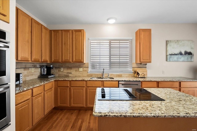 kitchen with decorative backsplash, wood finished floors, light stone countertops, stainless steel appliances, and a sink