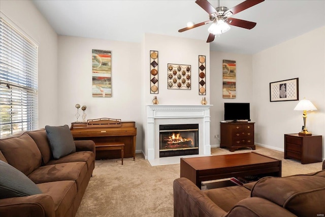 living area with light carpet, a fireplace with flush hearth, baseboards, and ceiling fan