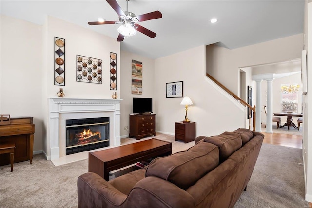 living area with ceiling fan, light colored carpet, a fireplace with flush hearth, baseboards, and stairway