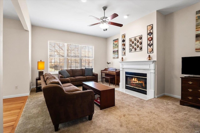 living area featuring a ceiling fan, a glass covered fireplace, and baseboards