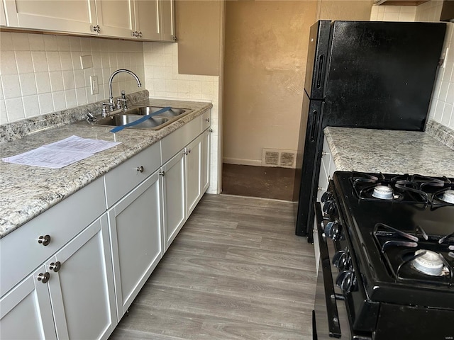 kitchen featuring black gas range oven, sink, light hardwood / wood-style floors, light stone countertops, and decorative backsplash