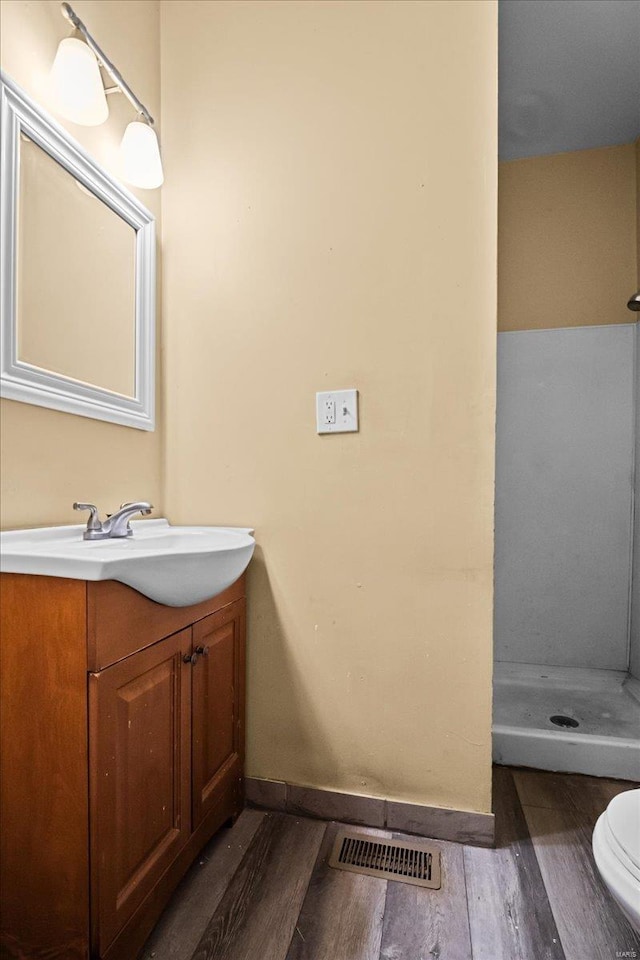 bathroom featuring vanity, wood-type flooring, a shower, and toilet