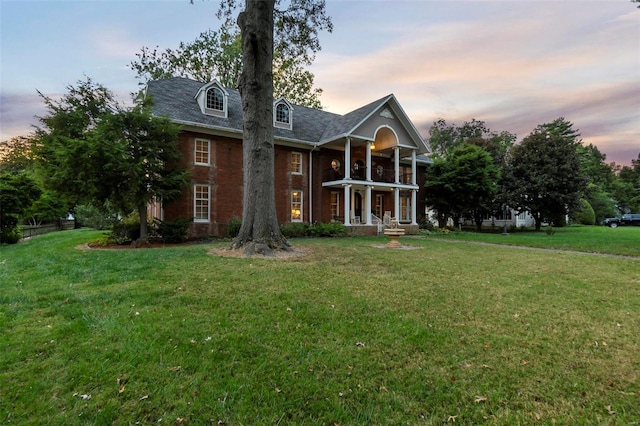 back house at dusk featuring a yard and a balcony