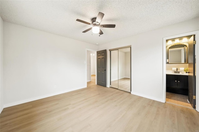 unfurnished bedroom with sink, light hardwood / wood-style floors, a textured ceiling, ensuite bath, and a closet