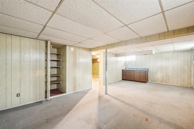 basement featuring a paneled ceiling, carpet, and wood walls