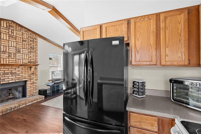 kitchen featuring lofted ceiling, range, black refrigerator, a fireplace, and wood-type flooring