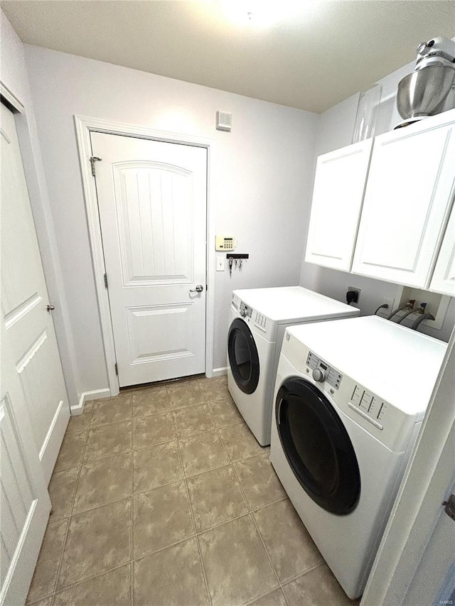 clothes washing area with washer and dryer, cabinets, and light tile patterned flooring