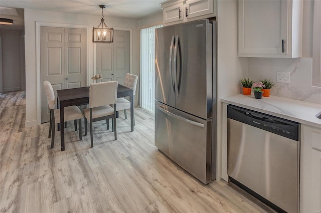 kitchen with white cabinetry, hanging light fixtures, stainless steel appliances, light stone countertops, and light hardwood / wood-style flooring