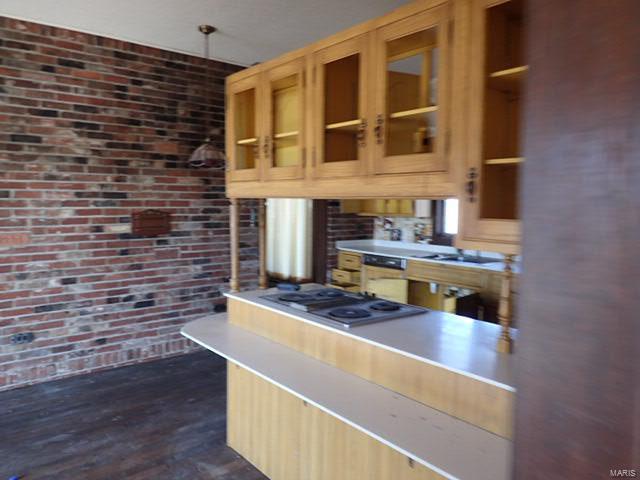 kitchen with dark wood-type flooring, stainless steel gas stovetop, and brick wall