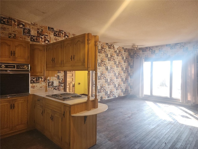 kitchen featuring black oven, dark hardwood / wood-style floors, a textured ceiling, kitchen peninsula, and stainless steel gas stovetop