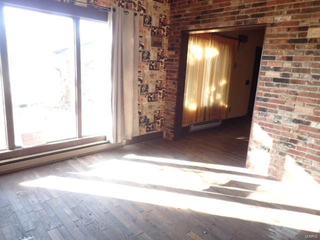 spare room featuring hardwood / wood-style flooring, a baseboard radiator, and brick wall