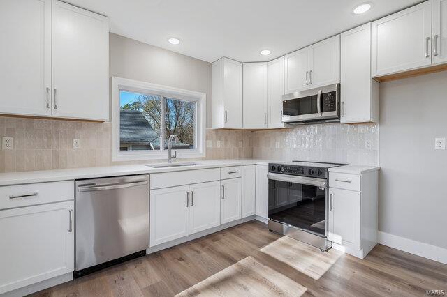 kitchen with sink, backsplash, stainless steel appliances, light hardwood / wood-style floors, and white cabinets