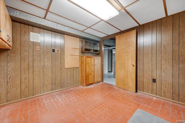 basement with a paneled ceiling, a wall mounted air conditioner, and wooden walls