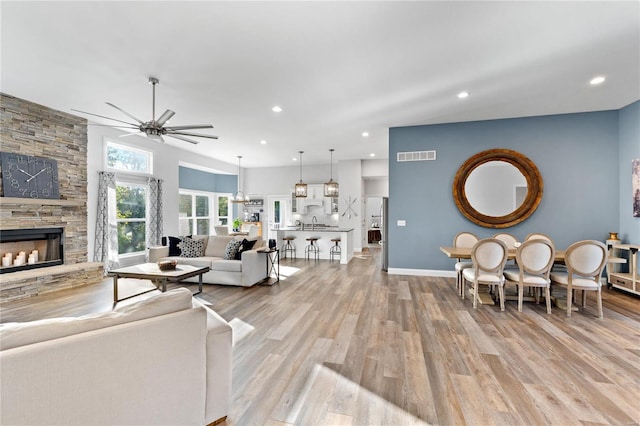 living room featuring ceiling fan, a stone fireplace, and light hardwood / wood-style floors