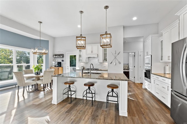 kitchen with a kitchen bar, dark stone countertops, an island with sink, stainless steel appliances, and white cabinets