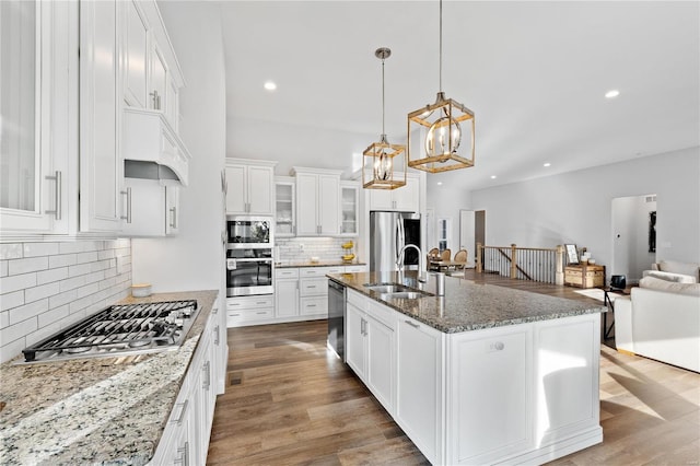 kitchen featuring stainless steel appliances, an island with sink, white cabinets, and decorative light fixtures