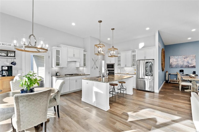 kitchen with appliances with stainless steel finishes, an island with sink, pendant lighting, dark stone counters, and white cabinets