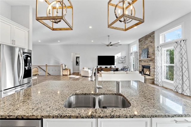 kitchen featuring stone countertops, stainless steel refrigerator, a fireplace, sink, and white cabinets