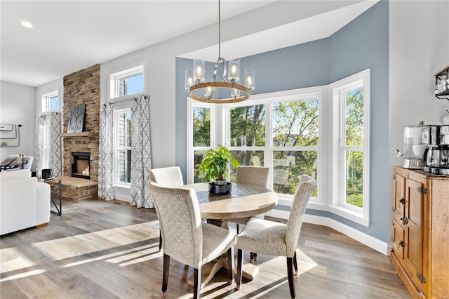 dining space with a notable chandelier, a stone fireplace, wood-type flooring, and a healthy amount of sunlight