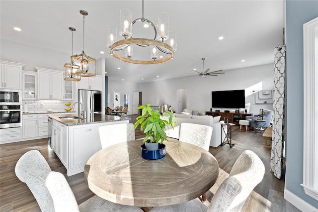 dining area with dark wood-type flooring, ceiling fan with notable chandelier, and sink