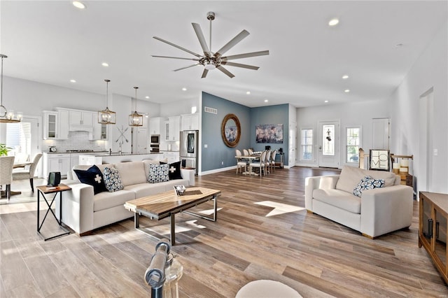 living room featuring sink, ceiling fan with notable chandelier, and light wood-type flooring