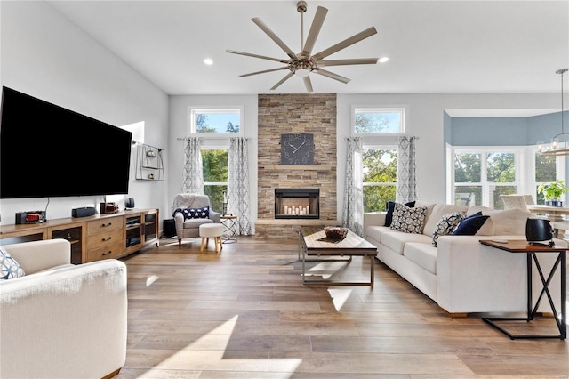 living room featuring a stone fireplace, ceiling fan with notable chandelier, and light hardwood / wood-style flooring