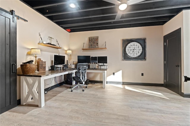 home office featuring beamed ceiling, a barn door, and light wood-type flooring