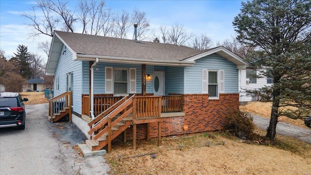 bungalow-style house with driveway, stairway, roof with shingles, a porch, and brick siding