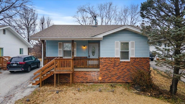 bungalow-style house featuring covered porch, a shingled roof, aphalt driveway, and brick siding