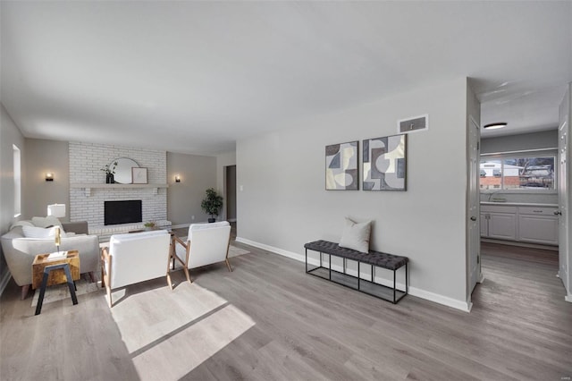 living room featuring light wood-style flooring, a brick fireplace, visible vents, and baseboards