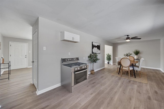 kitchen featuring dark countertops, light wood-style flooring, white cabinets, stainless steel gas range, and baseboards