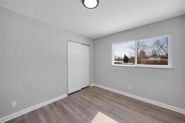 unfurnished bedroom with light wood-type flooring, a closet, and baseboards