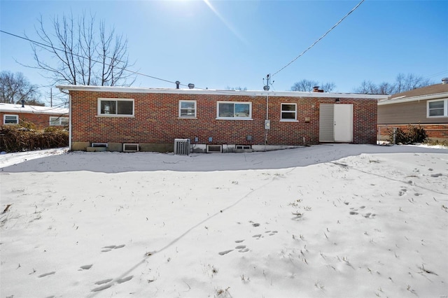 snow covered house featuring central AC and brick siding