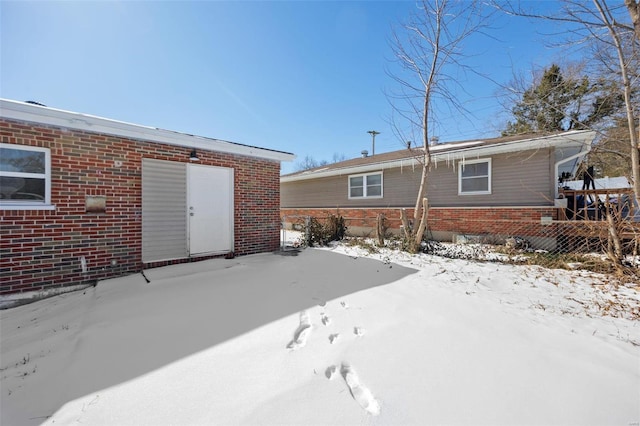 snow covered rear of property featuring brick siding and fence