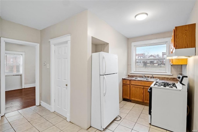 kitchen with brown cabinetry, range with gas stovetop, freestanding refrigerator, under cabinet range hood, and a sink