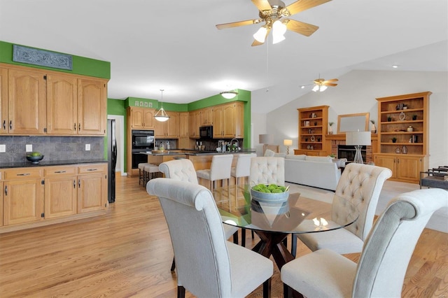 dining space featuring a fireplace, vaulted ceiling, ceiling fan, and light wood-type flooring