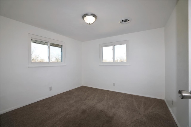 unfurnished room with visible vents, dark carpet, and baseboards